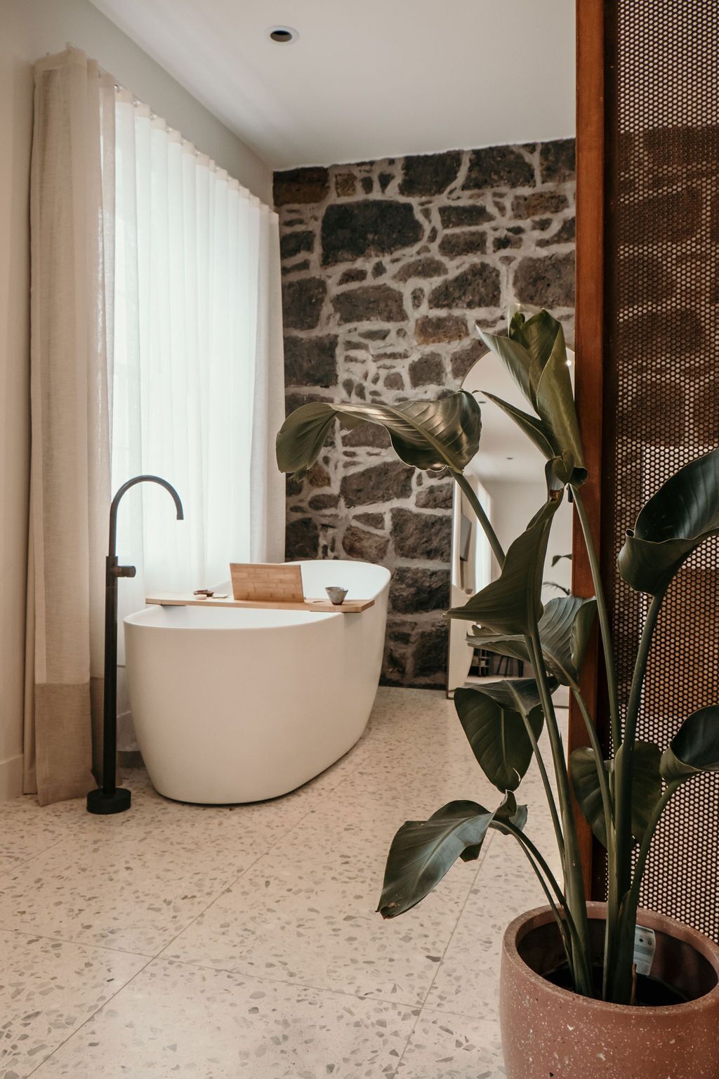 A bathroom with a freestanding bathtub, a potted plant, and a stone wall.