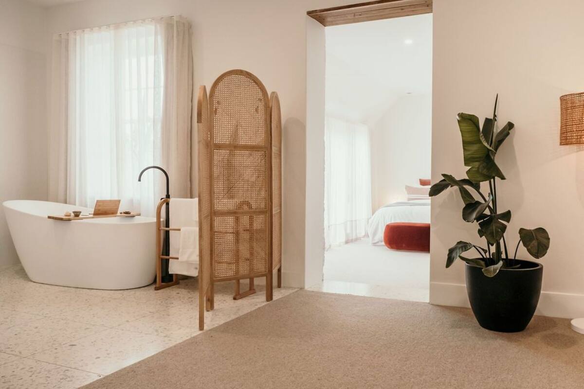 A modern bathroom with a freestanding bathtub, a wicker chair, and a potted plant.