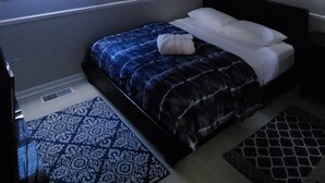 Un dormitorio con una cama, una ventana con cortinas, un ventilador de techo y una alfombra estampada.