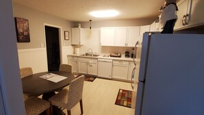 Una cocina compacta con armarios blancos, una mesa de comedor con sillas estampadas y un refrigerador.