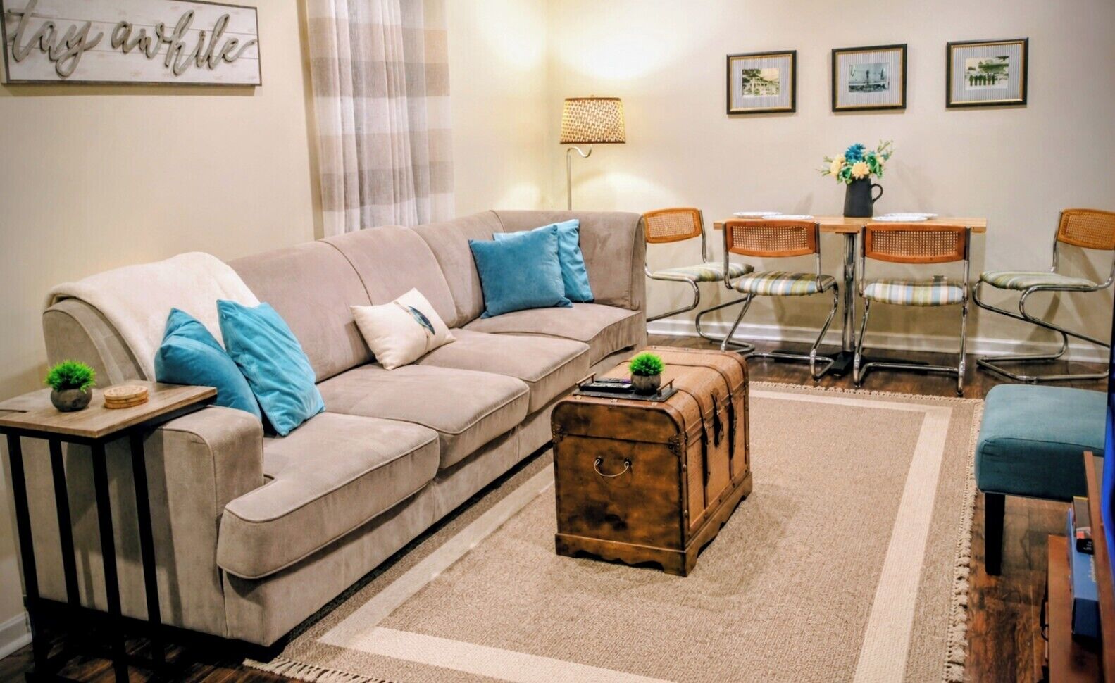 A living room with a sofa, a small table, a vintage suitcase, and a dining area with chairs and a table.
