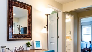 Una habitación con un escritorio de madera, una silla azul, un espejo grande y una cita enmarcada en la pared.
