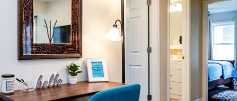 A room with a wooden desk, a blue chair, a large mirror, and a framed quote on the wall.