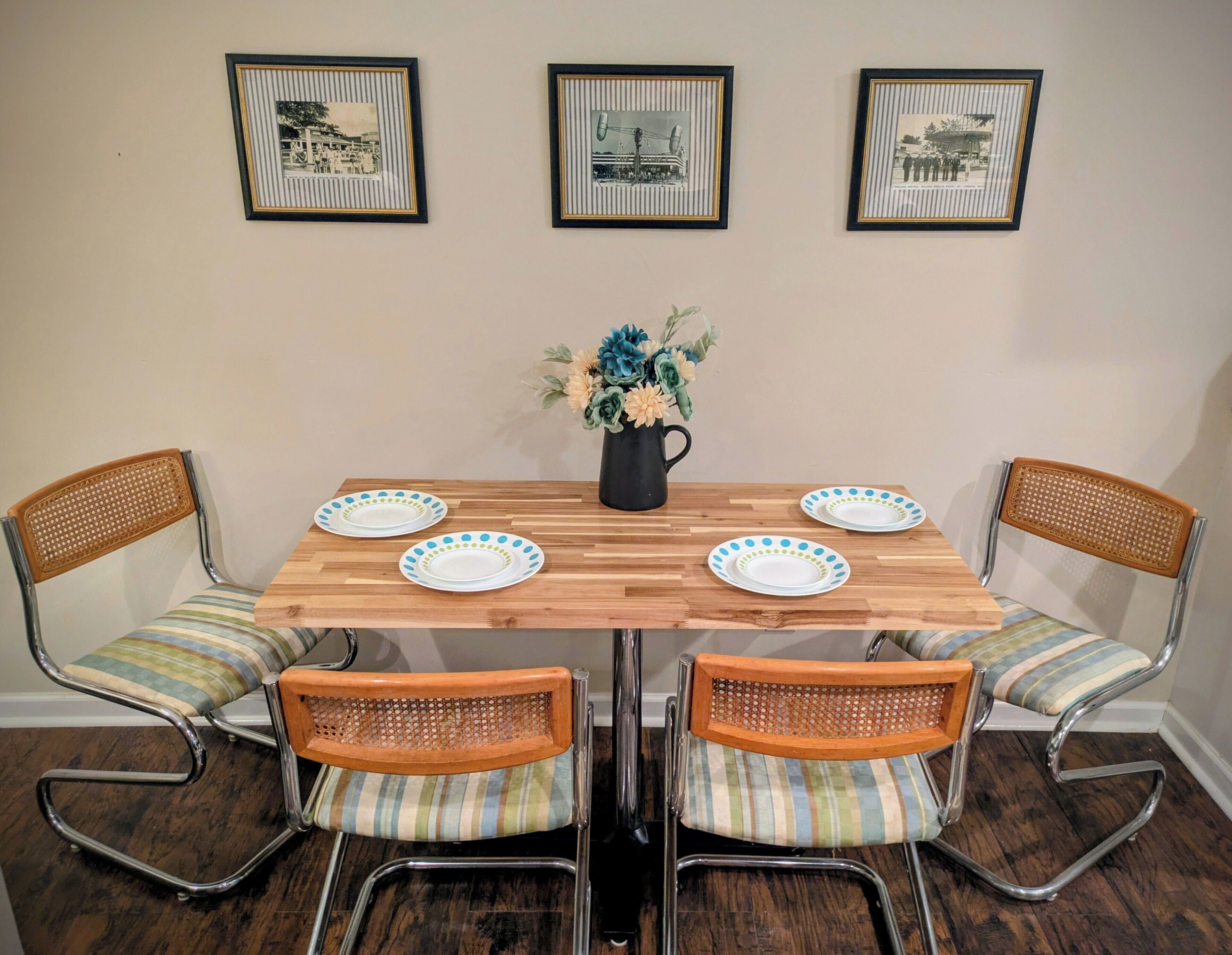 A dining table with four chairs, a vase with flowers, and three framed pictures on the wall.