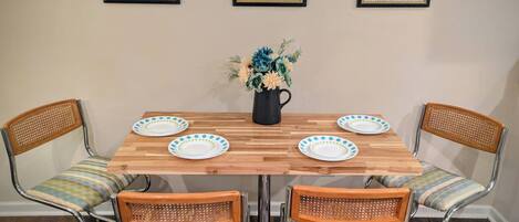 A dining table with four chairs, a vase with flowers, and three framed pictures on the wall.