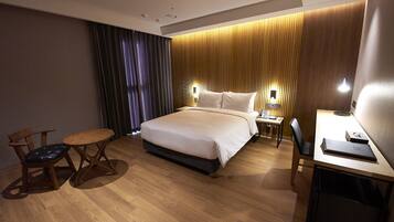 A hotel room with a large bed, a desk, a chair, and a small table.