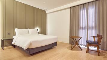 A modern hotel room with a large bed, a bedside table, a chair, and a small table.