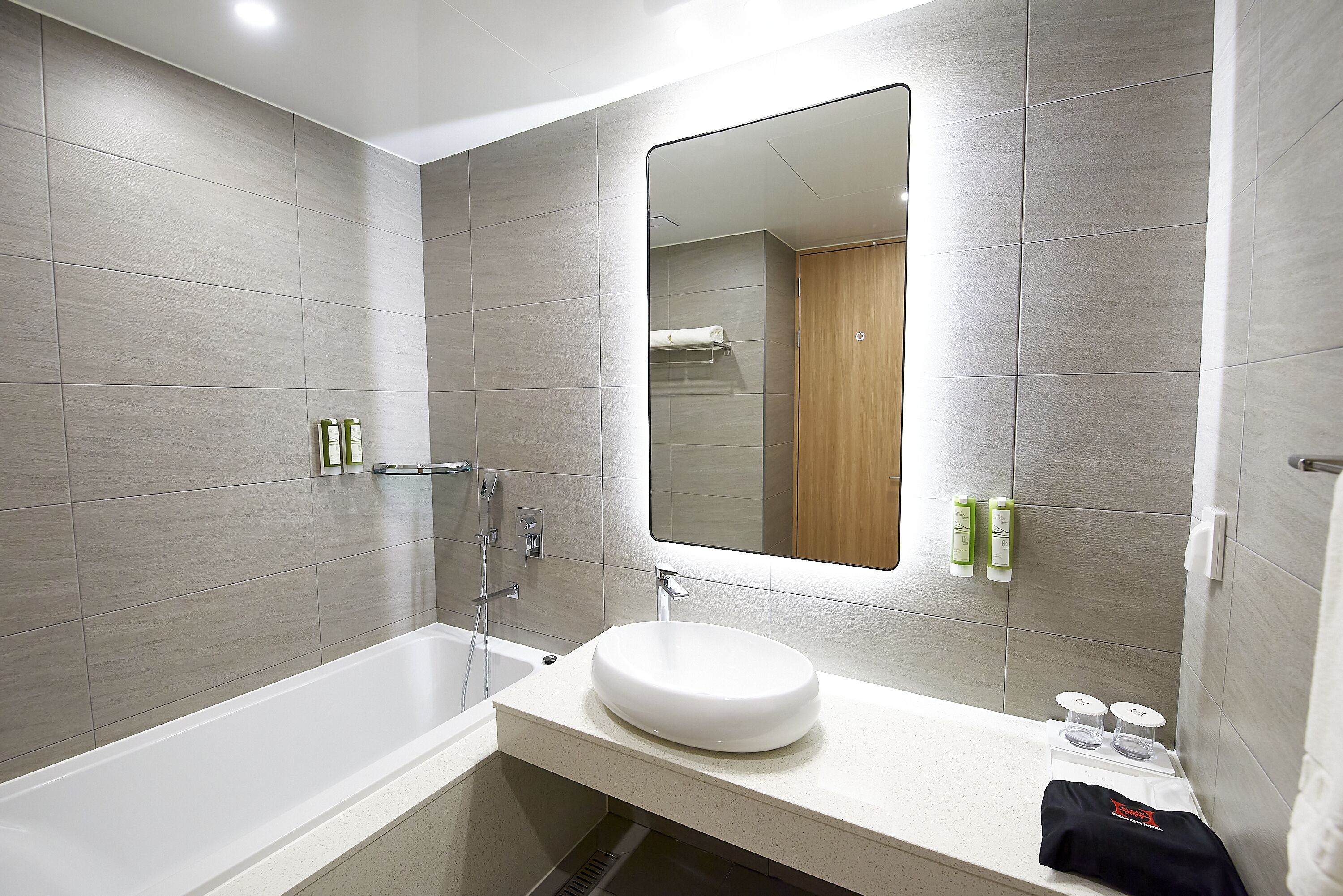 Un baño moderno con bañera, lavabo con espejo y artículos de aseo en la encimera.