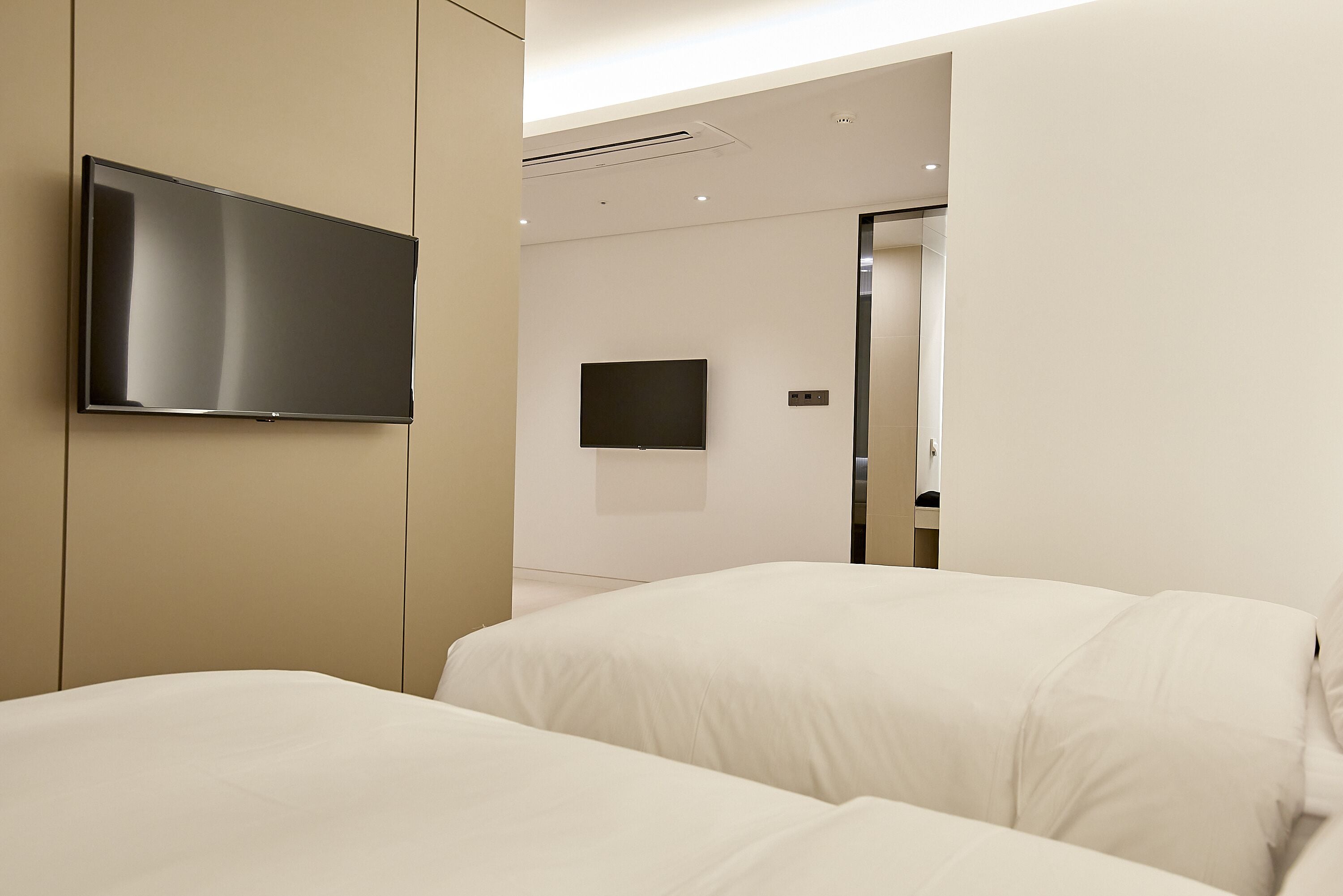 A modern hotel room with a large bed, a flat-screen TV mounted on the wall, and a small TV on the opposite wall.