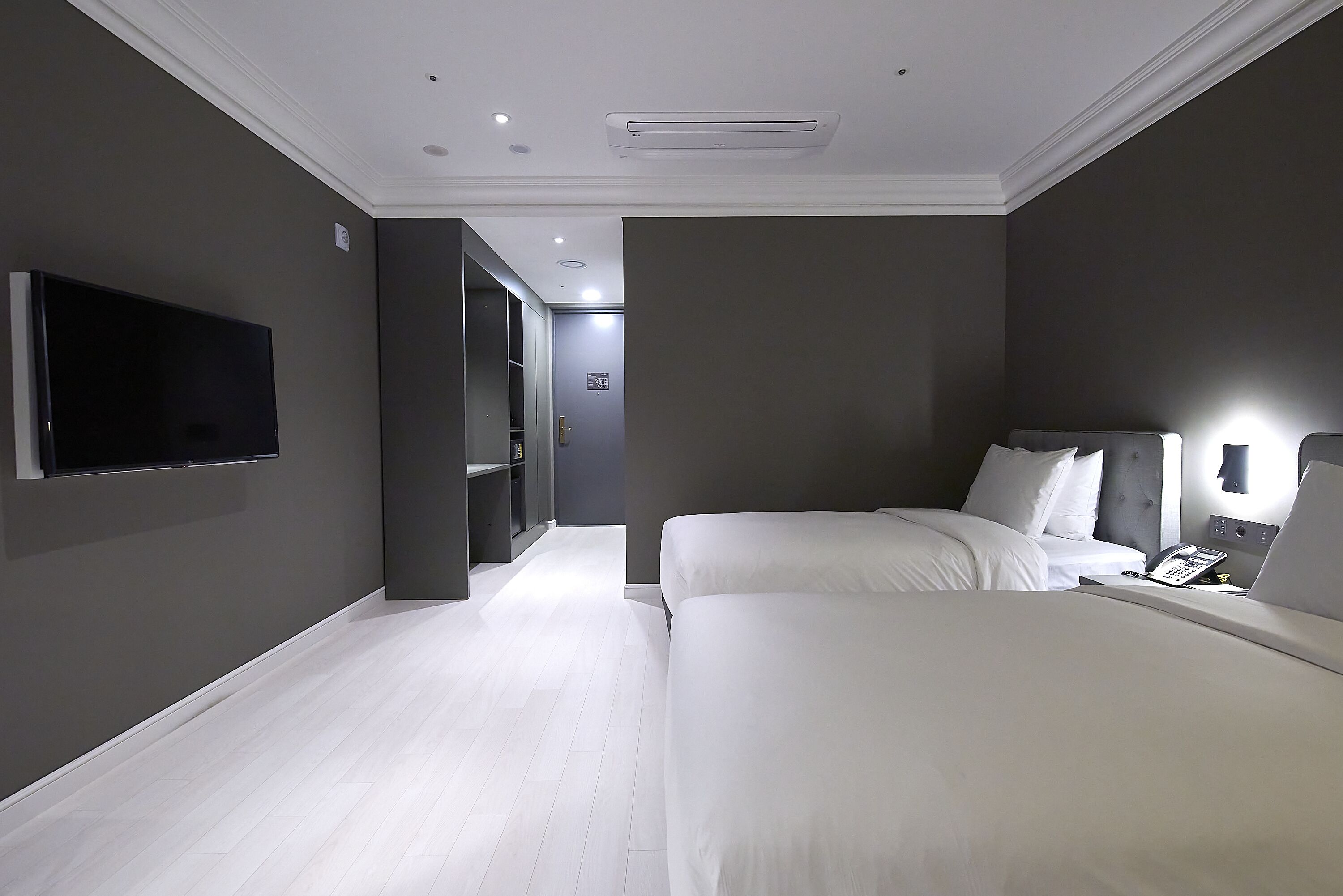 Une chambre d’hôtel moderne dotée d’un grand lit, d’un téléviseur à écran plat fixé au mur et d’une table de chevet avec une lampe.
