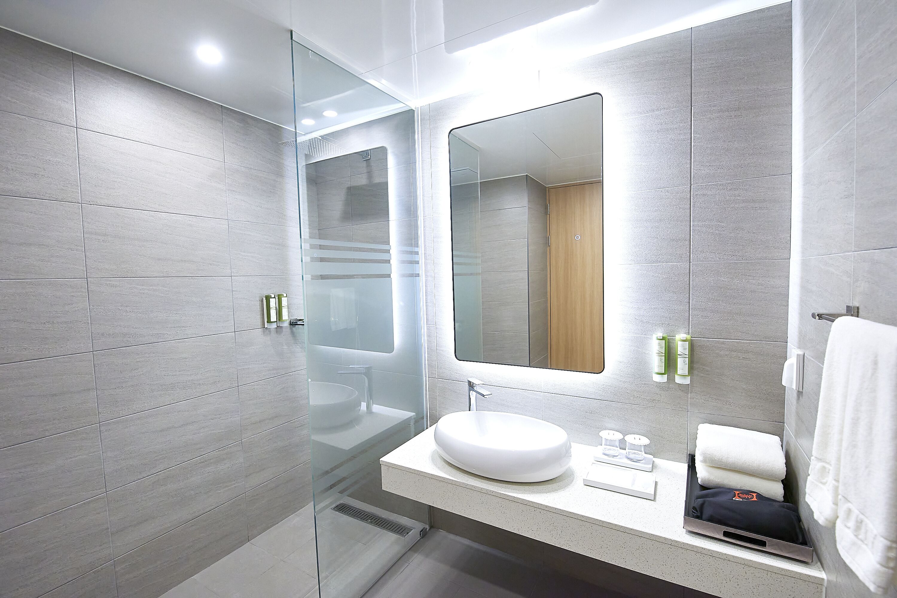 A modern bathroom with a glass shower enclosure, a white sink, and a large mirror above it.