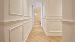 Un pasillo con paneles blancos y suelo de madera que conduce a una habitación con una puerta.
