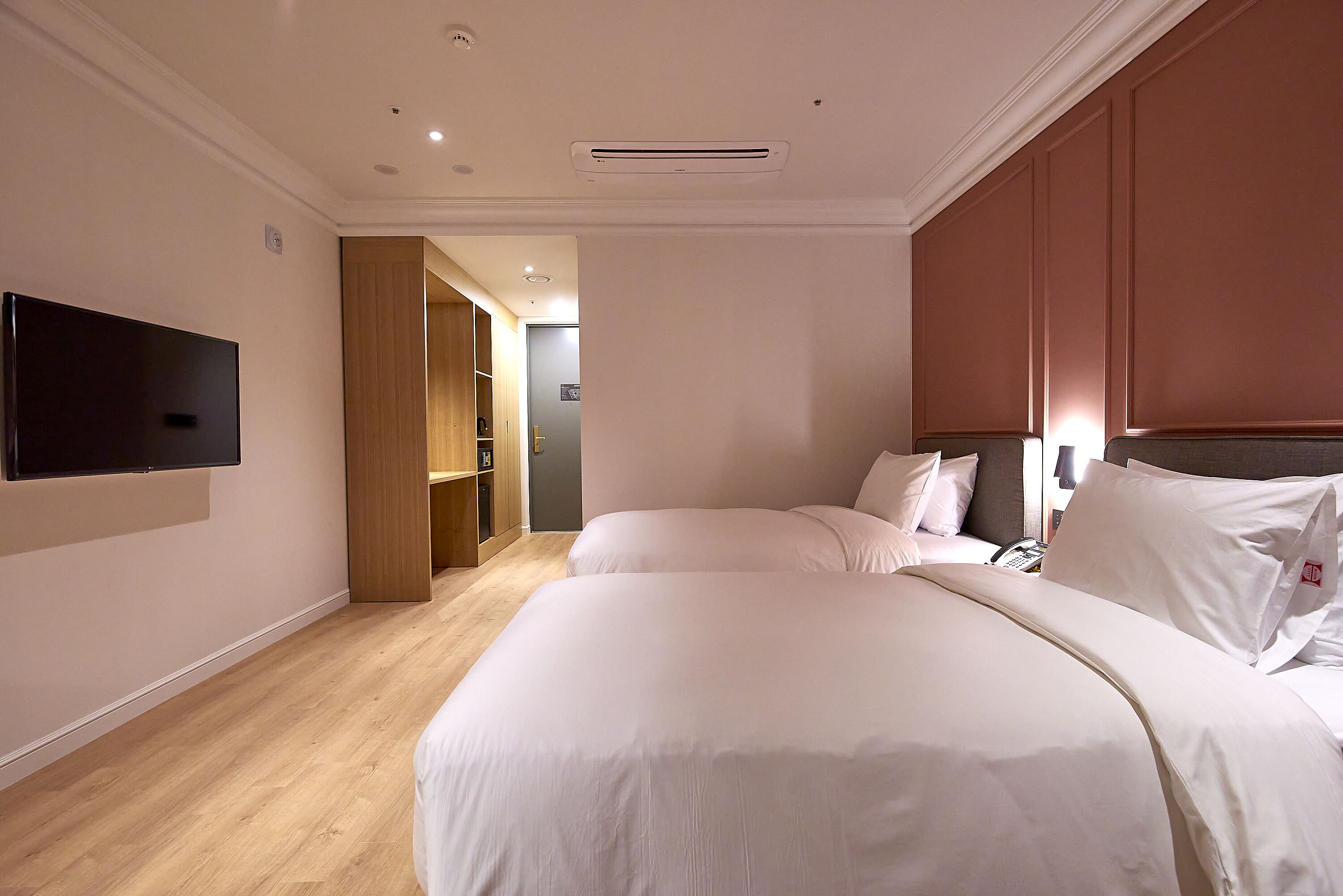 A hotel room with two beds, a TV mounted on the wall, and a wooden floor.
