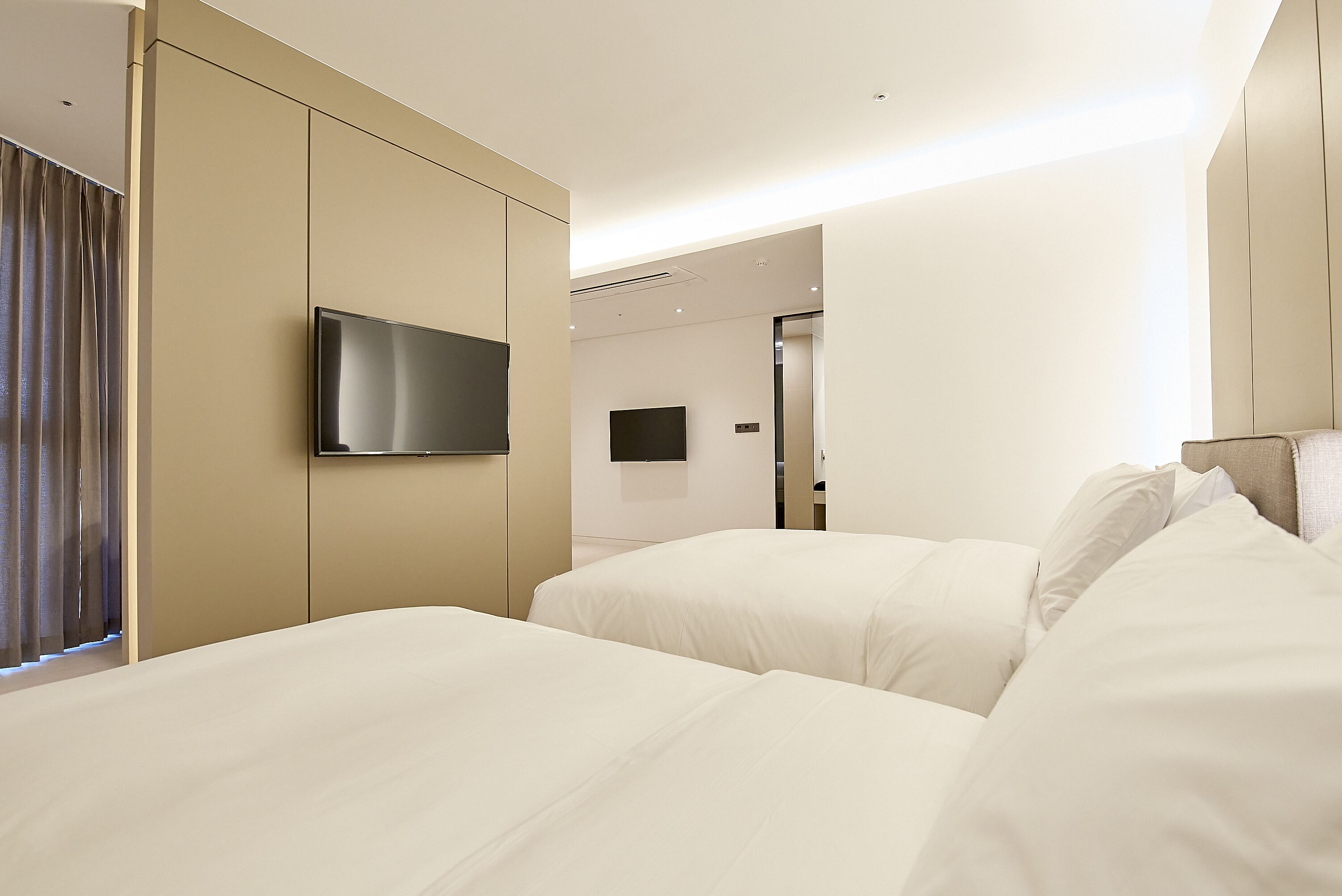 Habitación de hotel con dos camas, un televisor de pantalla plana montado en la pared y una puerta que da al baño.