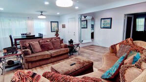 A spacious living room with a brown sofa, a coffee table, and a dining area with a table and chairs. - Historic Renovated Kemah Home just a short walk to the Kemah Boardwalk. (Kemah)