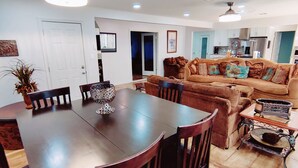 A dining area with a wooden table and chairs, a sofa, and a kitchen in the background. - Historic Renovated Kemah Home just a short walk to the Kemah Boardwalk. (Kemah)