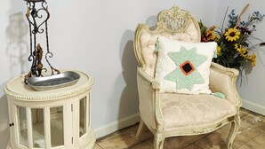 A vintage-style chair with a decorative pillow, a small side table with a candle holder, and a vase with flowers. - Historic Renovated Kemah Home just a short walk to the Kemah Boardwalk. (Kemah)