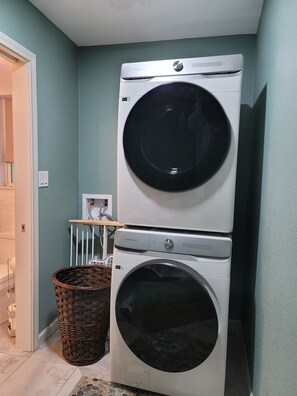 Une buanderie équipée de deux machines à laver à chargement frontal superposées, d’un panier en osier et d’une porte blanche.