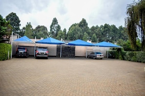 A parking area with three cars under blue canopies, surrounded by greenery and trees. - Simba Village Relax Inn (Eldoret)