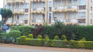 A multi-story hotel with balconies and a well-maintained garden in front. - Simba Village Relax Inn (Eldoret)