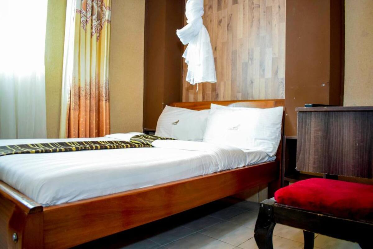 A neatly made bed with white linens and a striped blanket, a wooden headboard, and a red cushioned chair.