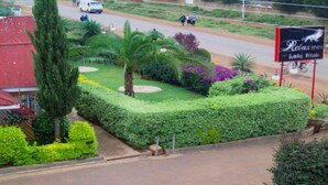 A landscaped garden with neatly trimmed hedges, a palm tree, and a sign for Relaxinn Simba Village. - Simba Village Relax Inn (Eldoret)
