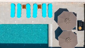 A rooftop pool with six blue lounge chairs and two large umbrellas. - Villa Divina PoolFront Suites (Kremasti)