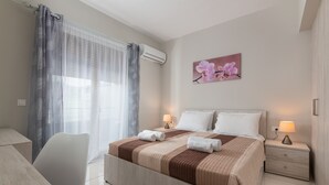 A neatly arranged bedroom with a bed, bedside tables, a chair, and a window with curtains. - Villa Divina PoolFront Suites (Kremasti)