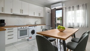 A modern kitchen with white cabinets, a wooden countertop, a built-in oven, a washing machine, and a dining area with a table and chairs. - Villa Divina PoolFront Suites (Kremasti)