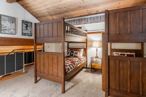 Una litera con estructura de madera, una mesita con lámpara y dos cuadros en la pared.