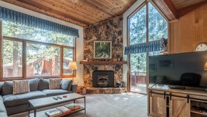 A cozy living room with a stone fireplace, a large TV, and a comfortable sofa. - Spacious Winterset 26 2 Bedrm Plus Loft 3 Full Bathrm Townhome Sleeps 8 Steps to Free Town Shuttle (Mammoth Lakes)