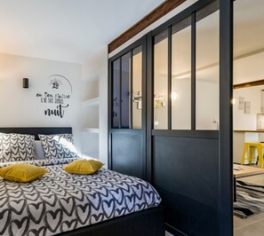 Quarto com cama, roupa de cama com padrão de coração, parede com frase em francês e porta de correr.