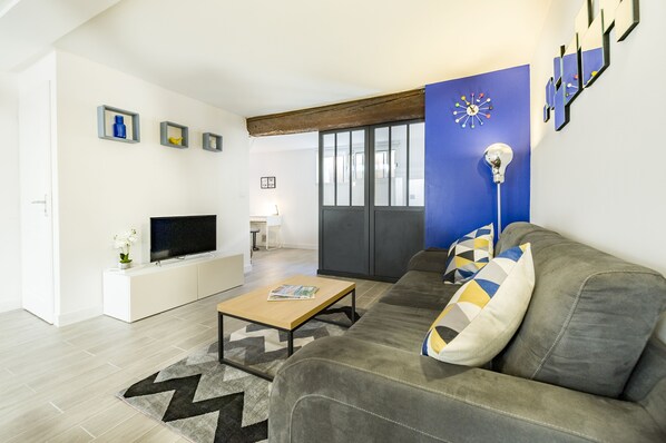 Uma sala de estar moderna com um sofá cinza, uma mesa de centro, uma televisão de tela plana e uma parede azul de destaque.