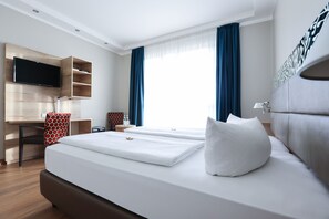 A modern hotel room with a large bed, a desk with a flat-screen TV, and a window with blue curtains. - Hotel Blaubeurer Tor (Ulm)