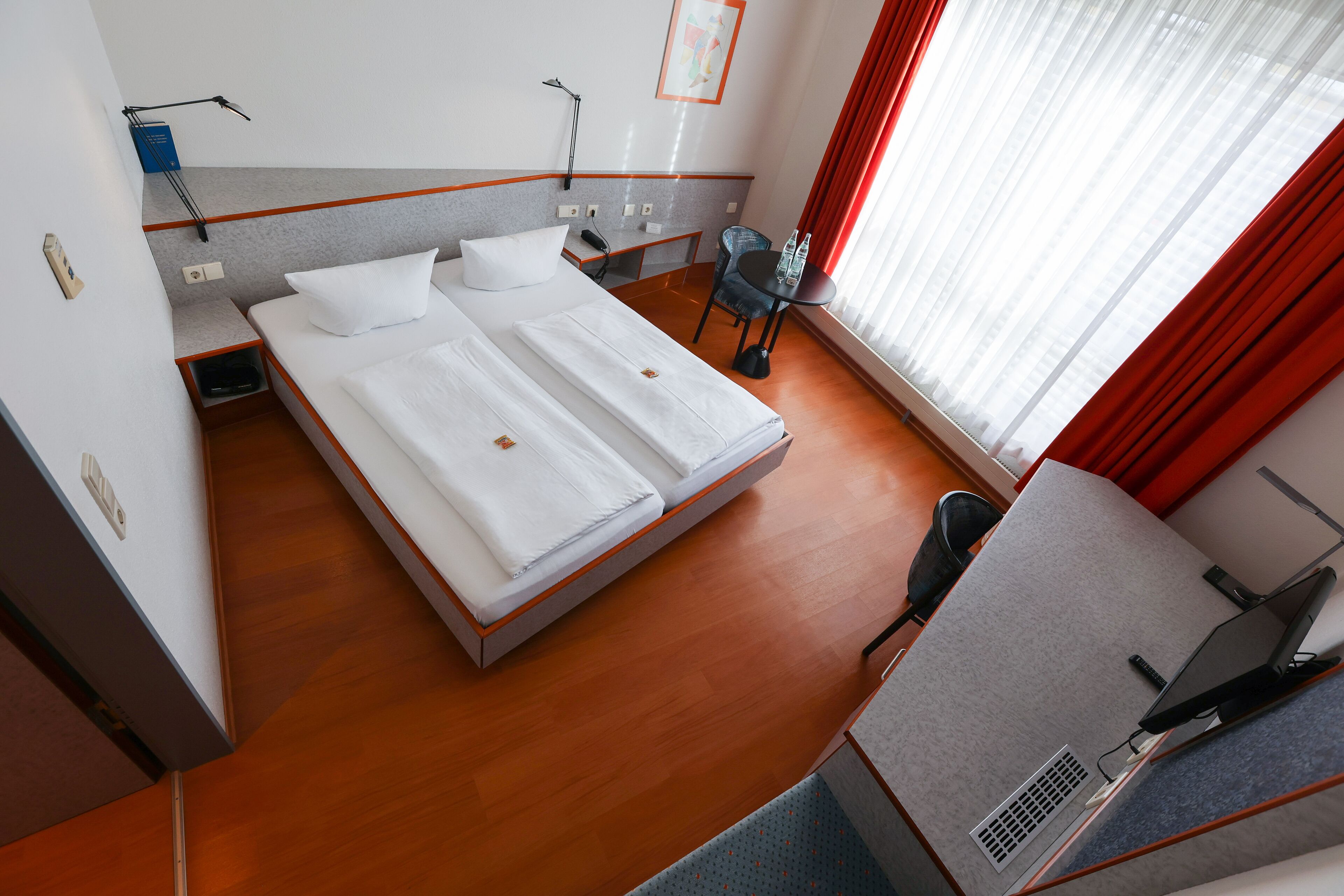 A hotel room with a large bed, a desk with a computer, a chair, and a window with curtains.