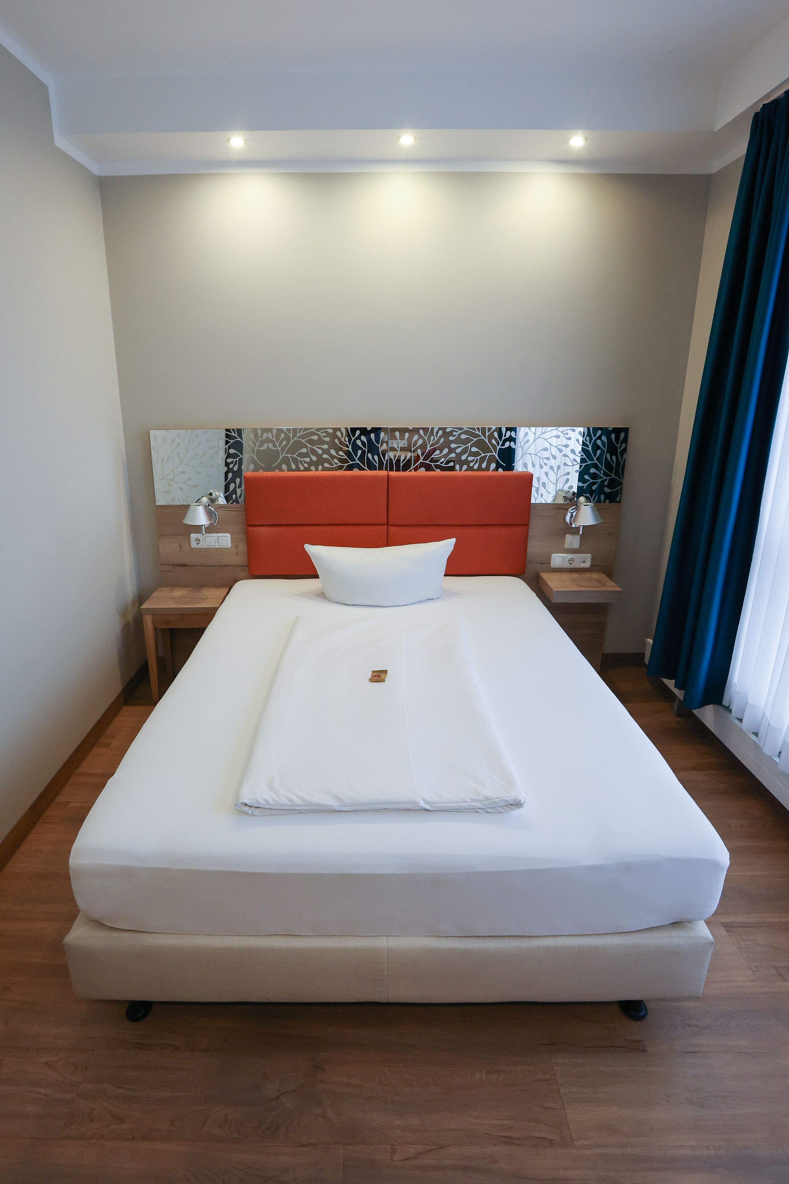 A neatly made bed with a white mattress and pillows, a wooden headboard, and a nightstand with a lamp.