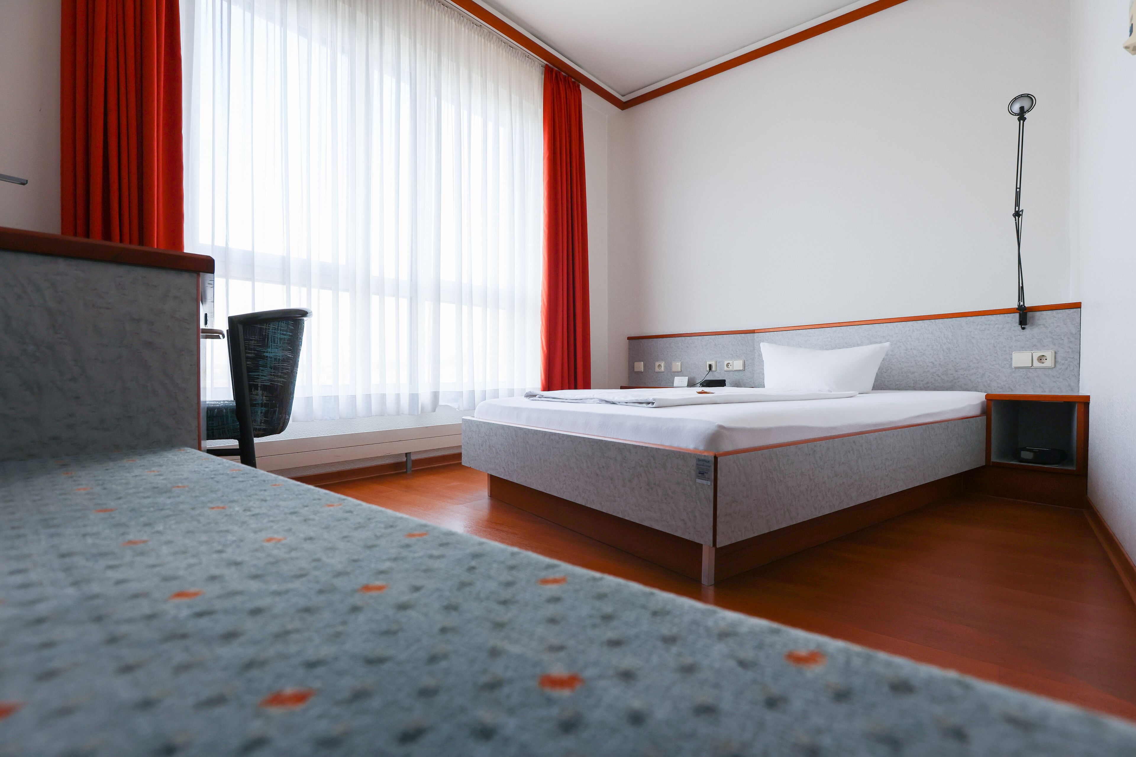 A hotel room with a bed, a chair, a desk, and a window with curtains.
