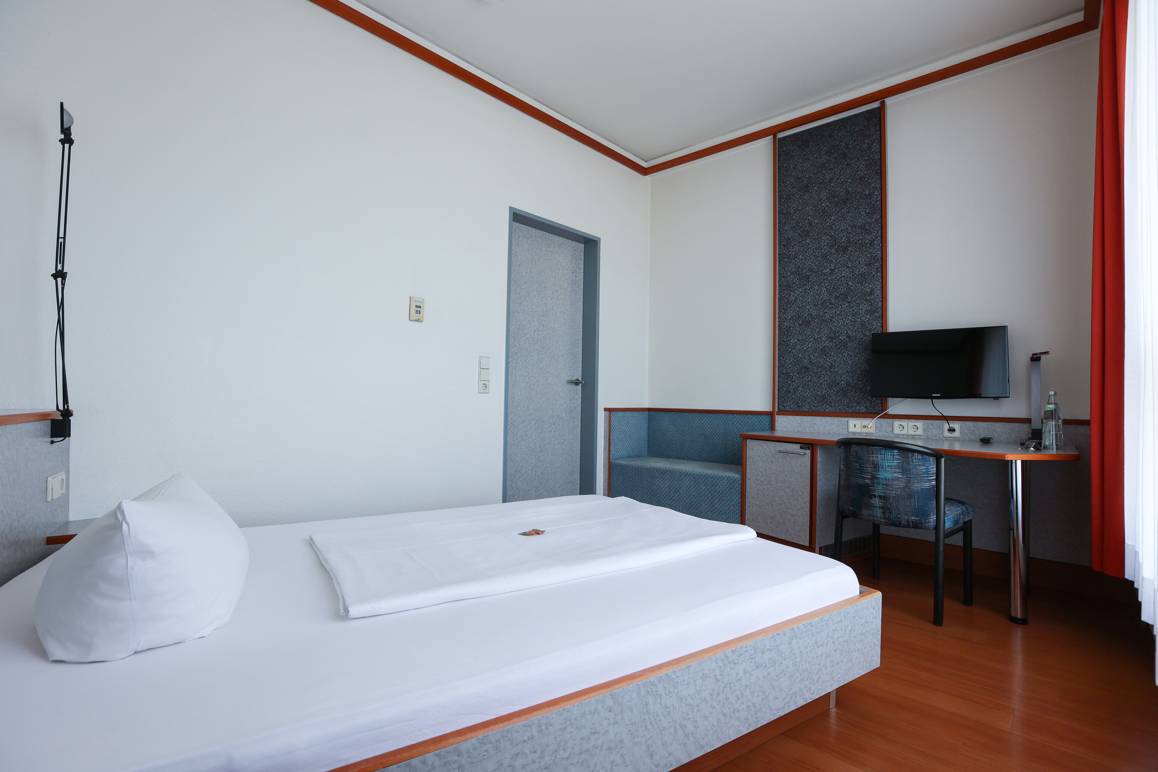 A hotel room with a bed, a desk, a chair, a television, and a door.