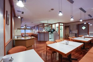 A restaurant with wooden tables and chairs, a kitchen area, and a counter with various items. - Hotel Blaubeurer Tor (Ulm)