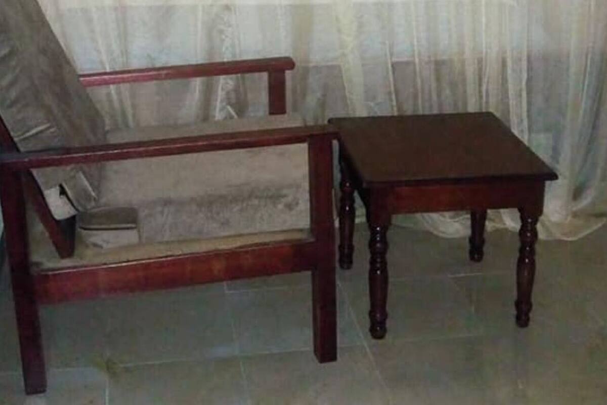 A room with a bed covered by a sheer white curtain, a wooden chair, and a small wooden table.