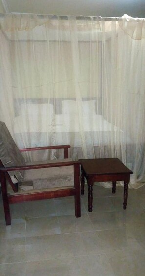 A room with a bed covered by a sheer white curtain, a wooden chair, and a small wooden table. - Lalwa Safari Lodge (Kabarnet)