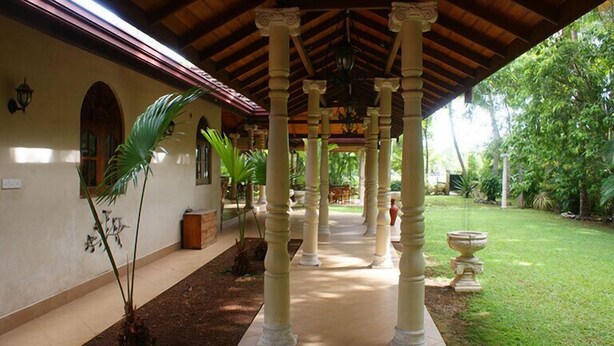 A covered outdoor area with columns, a pathway, and a garden with trees and plants. - Dedduwa Boat House (Bentota)