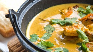 A black cast iron skillet filled with a creamy curry dish garnished with cilantro, placed on a wooden board. - Dedduwa Boat House (Bentota)