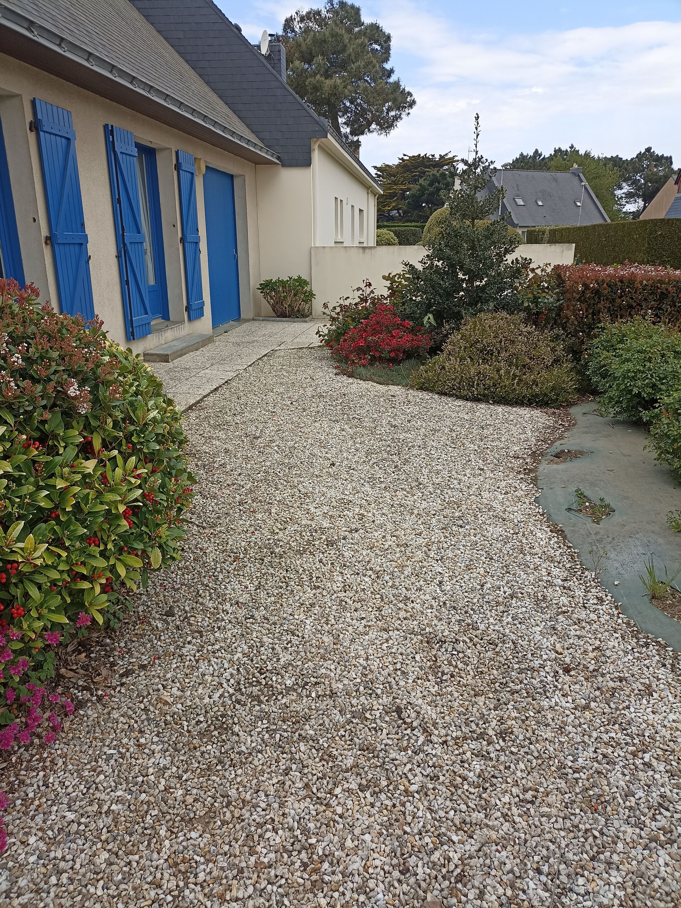 A gravel driveway leading to a building with blue shutters and a beige facade.