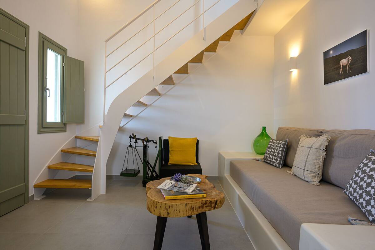 A modern living room with a staircase, a sofa, a coffee table, and a painting on the wall.