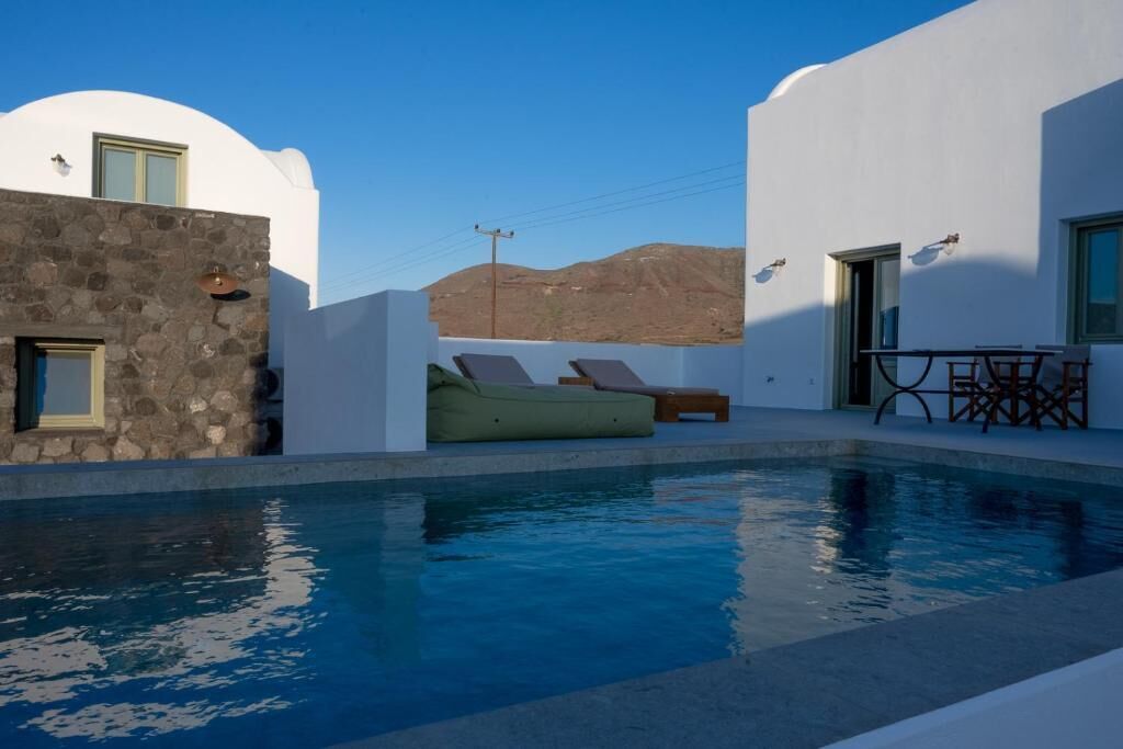 A pool area with a stone wall, a green lounge chair, and a table with chairs.