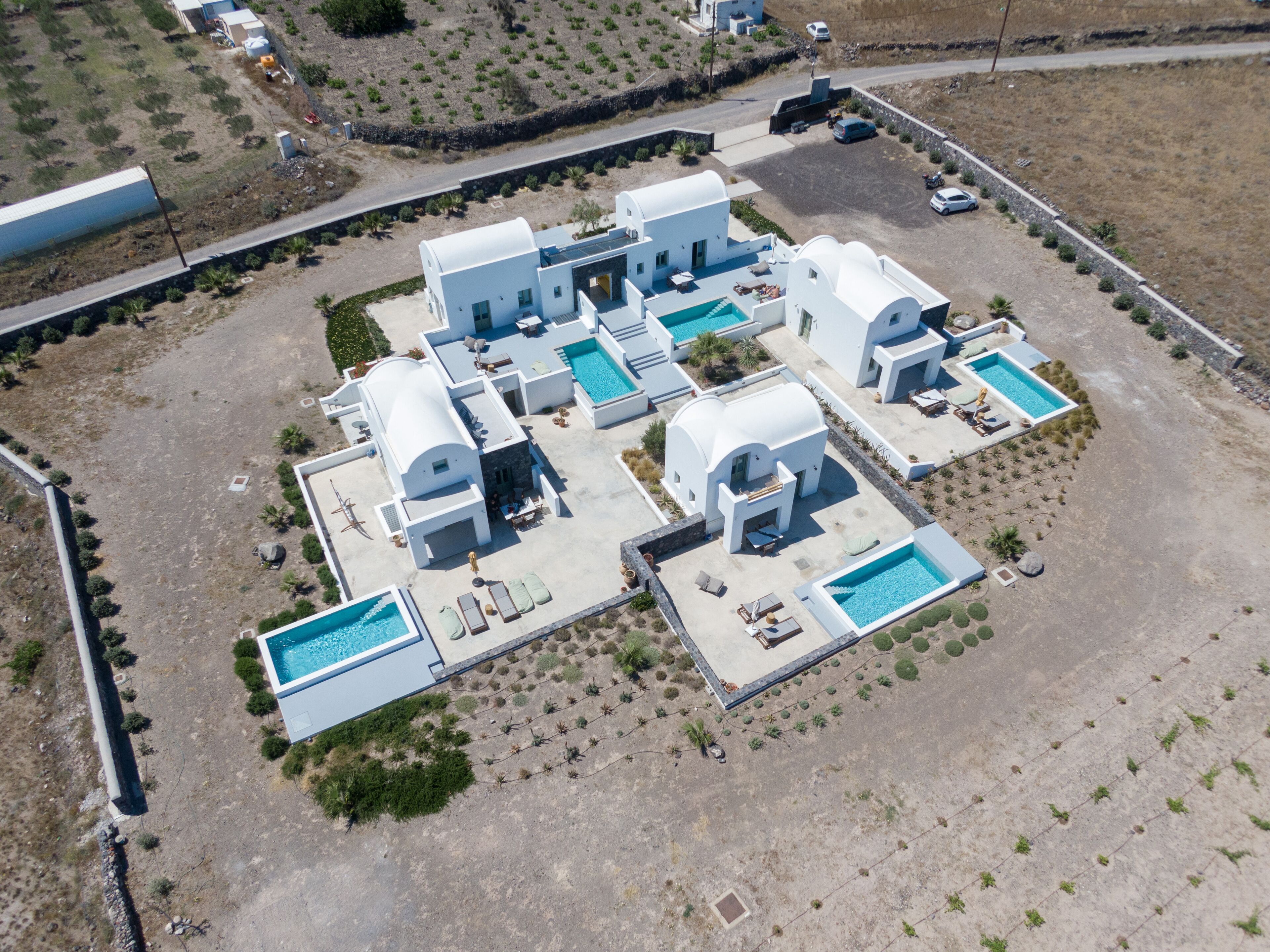 An aerial view of a modern resort with multiple white buildings, swimming pools, and landscaped areas.