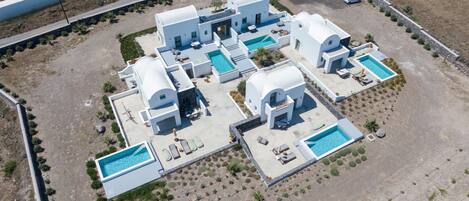 An aerial view of a modern resort with multiple white buildings, swimming pools, and landscaped areas.