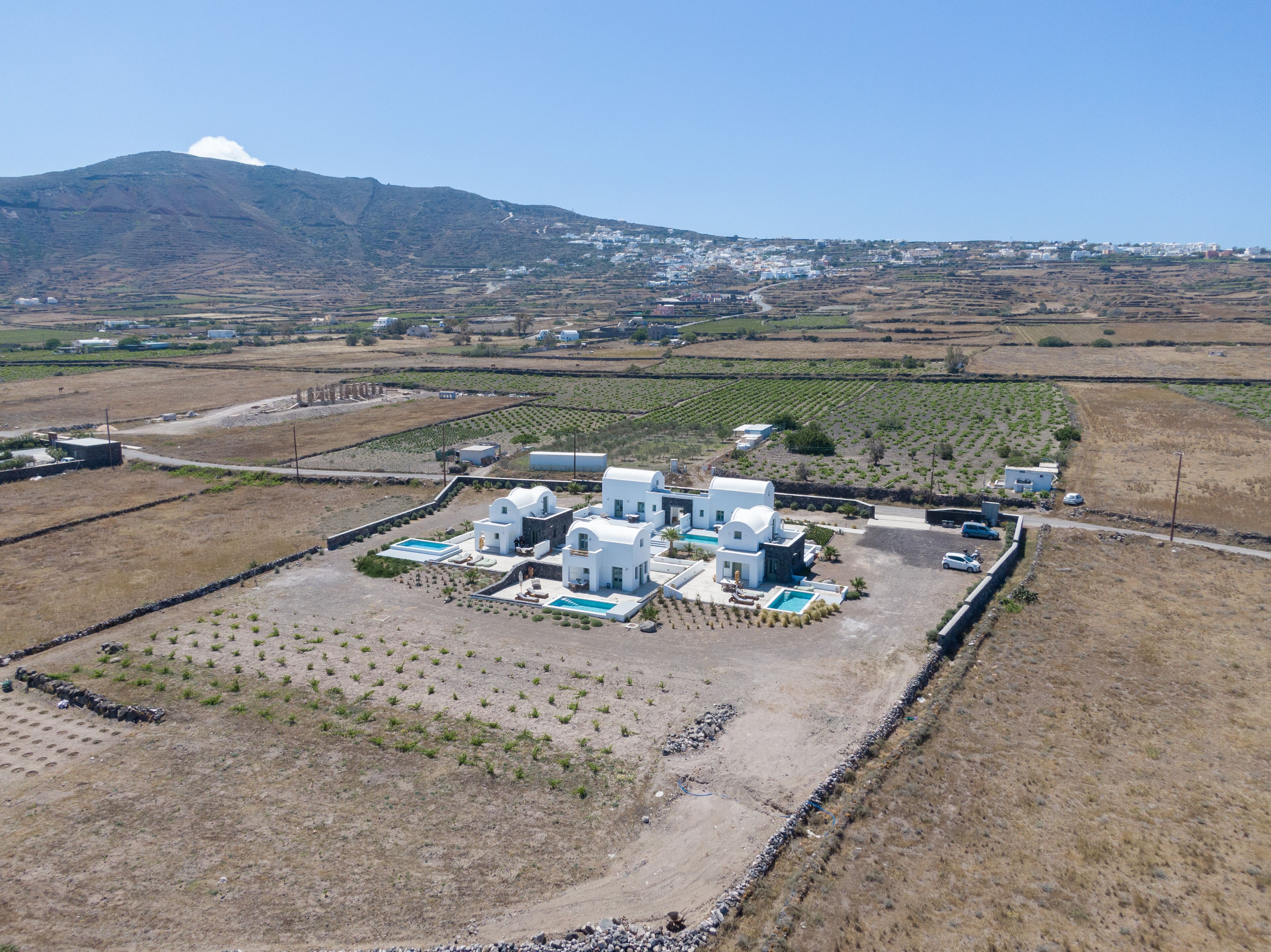 A white villa with a pool, surrounded by fields and a mountain in the background.