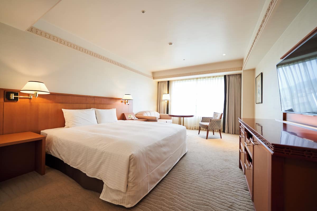 Ein Hotelzimmer mit einem großen Bett, Nachttischen, einem Schreibtisch, einem Stuhl und einem Fernseher.